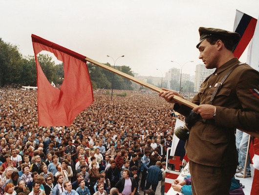 Russian soldier holding torn Russian flag above crowd of people