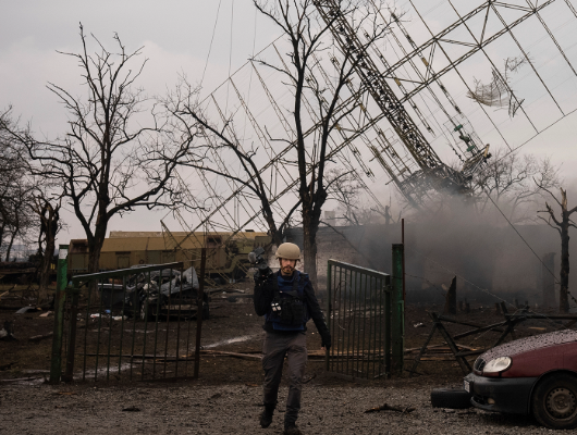 A journalist carries a camera while walking through a war zone