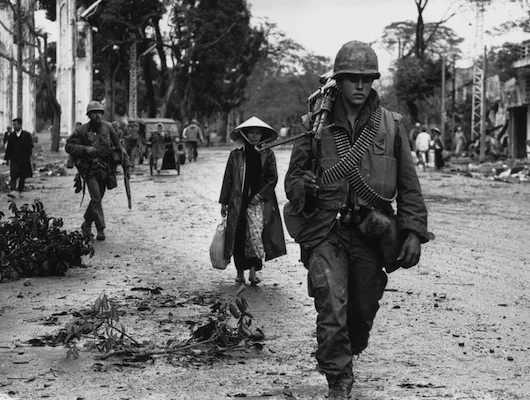 U.S. soldier walks down dirt road with Vietnamese people