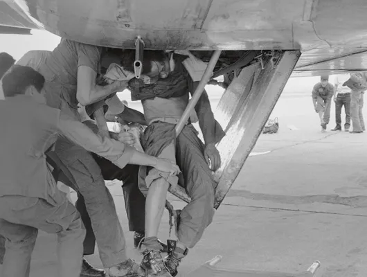 Soldiers help a man clinging to the wheel carriage of a plane