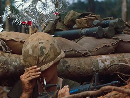 Armed soldier in trench with a Christmas tree behind him