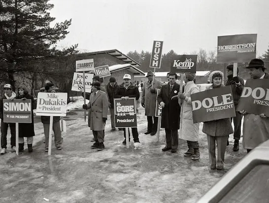 People standing in a frozen parking lot holding signs supporting their favorite presidential candidate