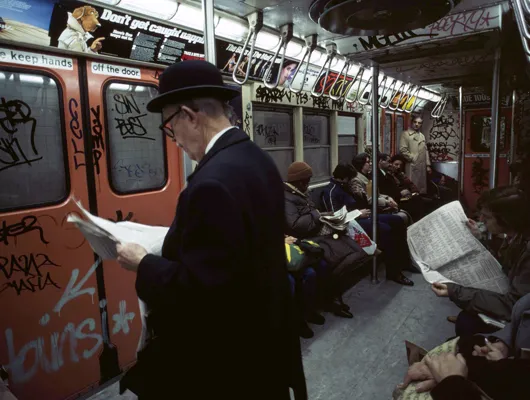 Graffiti-covered interior of subway car with passengers reading newspapers