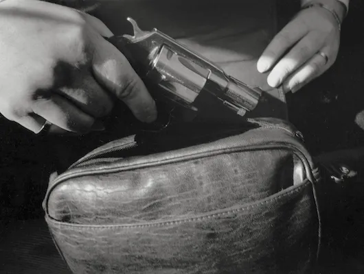 hands grip a pistol near a satchel