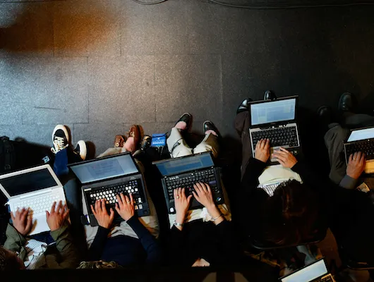 overhead shot of people typing on laptop computers in a lecture hall