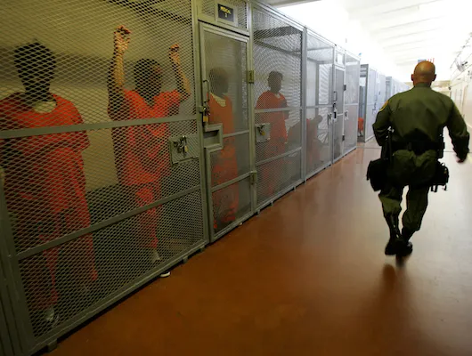 Guard walking by jailed inmates in orange jumpsuits