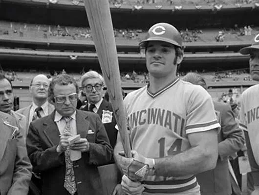 Pete Rose holding a bat surrounded by media 