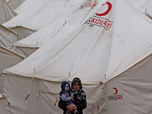 Woman holds child while standing amid tents for refugees 