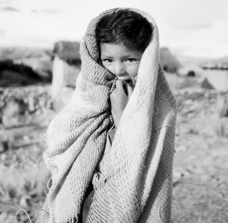 Altiplano Altiplano, Bolivia. A girl stays warm under a home-knitted shawl in late afternoon cold mountain Bolivian air.