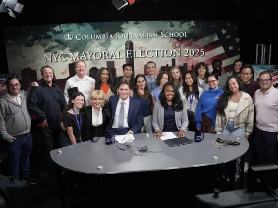 Students gathered behind a broadcast table in the CJS broadcast studio. 